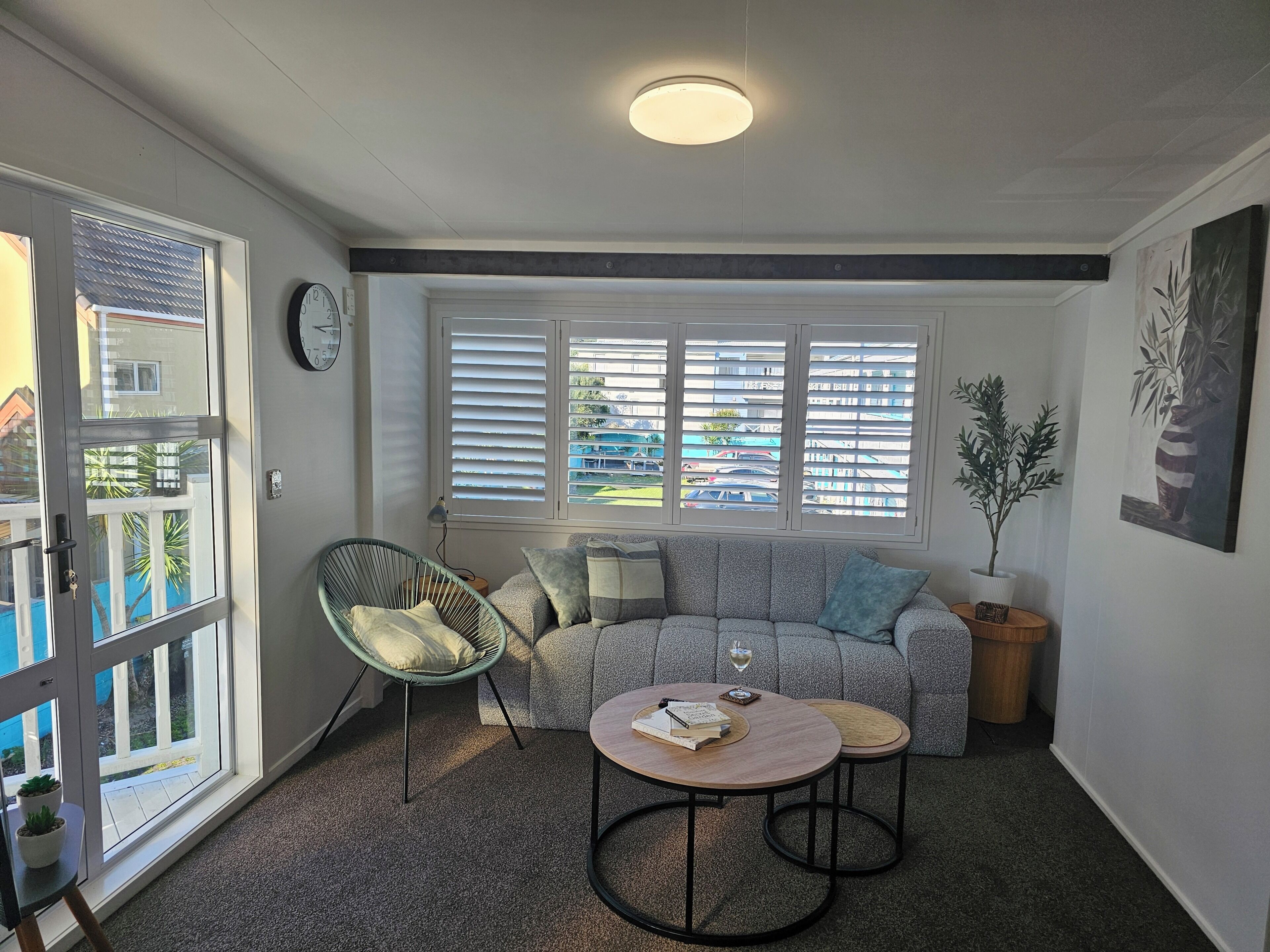 Un salón con un sofá, dos mesitas auxiliares, una silla, una planta en maceta y vistas al exterior.