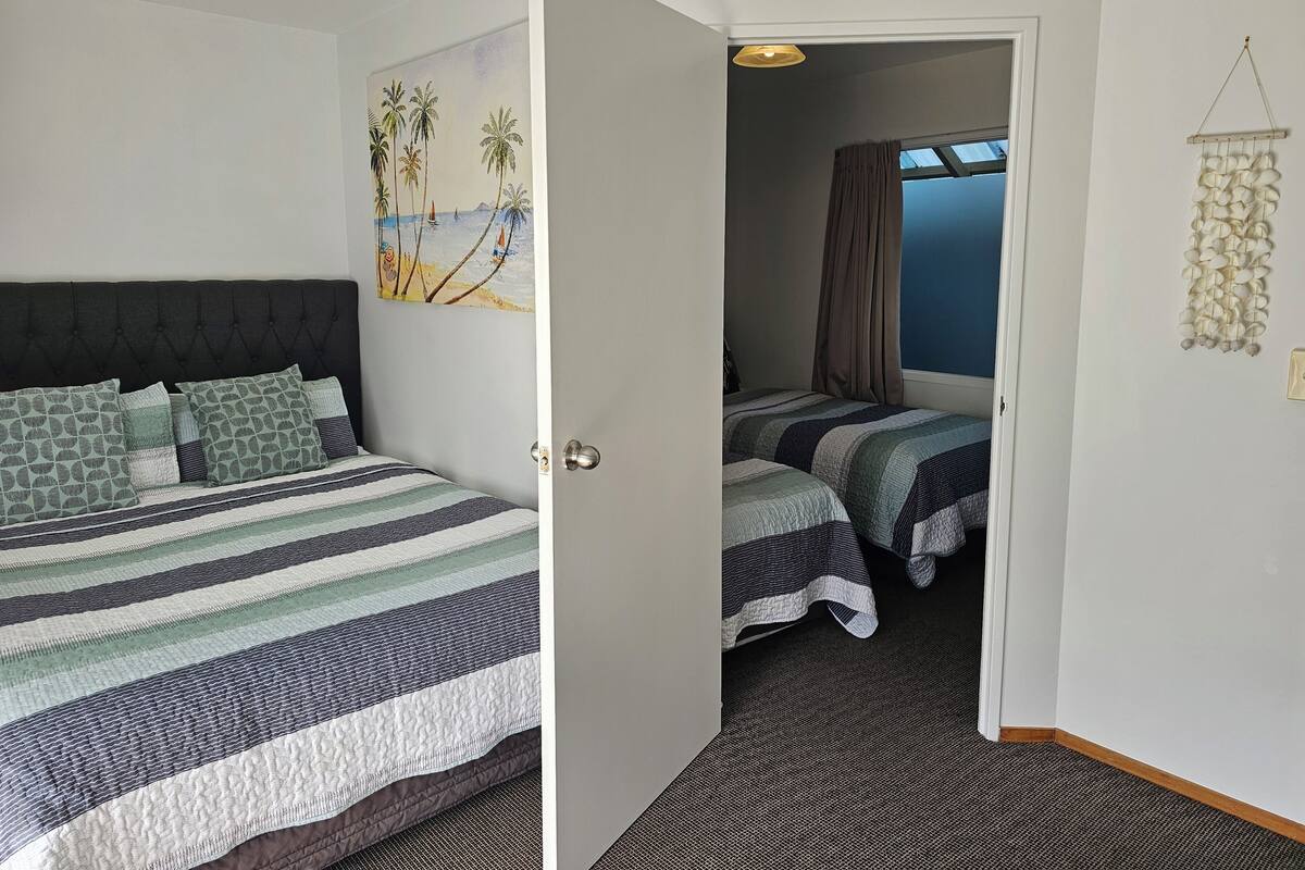 Une chambre d’hôtel avec un lit, un deuxième lit, un tableau, une porte et une vue sur la mer.