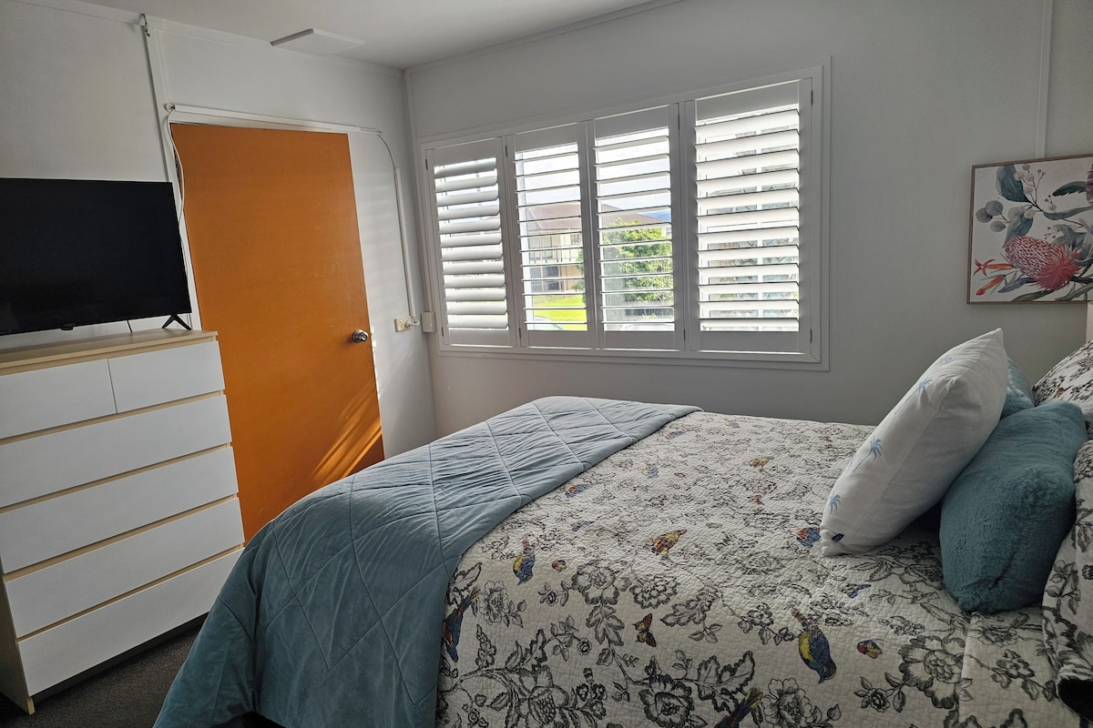 A bedroom with a bed, a dresser, a television, and a window with blinds.