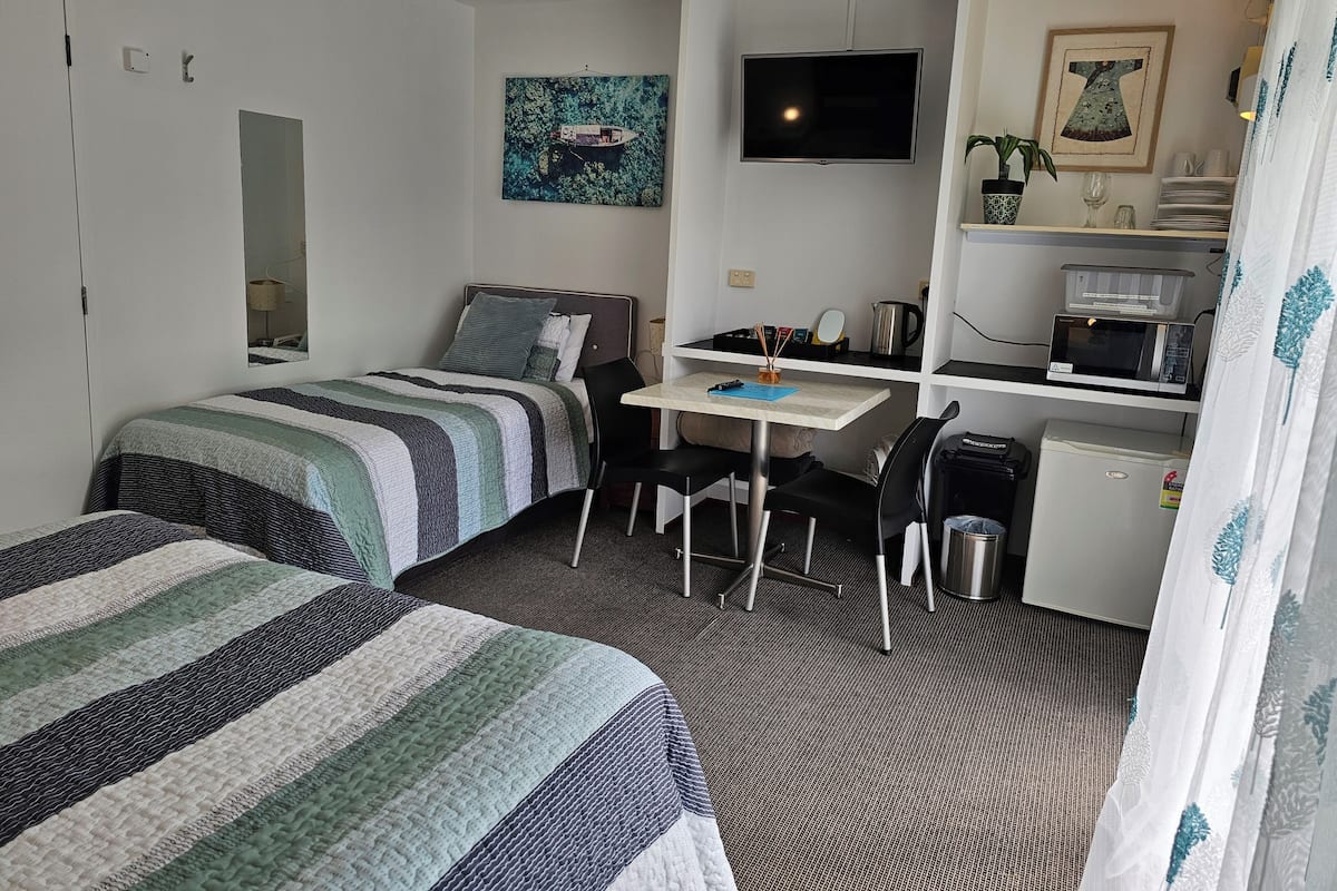 Une chambre d’hôtel avec deux lits, un bureau, une télévision, un petit réfrigérateur et un four à micro-ondes.