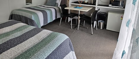 Habitación de hotel con dos camas, un escritorio, un televisor, un refrigerador pequeño y un microondas.