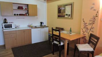 A compact kitchen with a microwave, sink, and wooden cabinets. There is a dining table with chairs and a small rug on the floor.