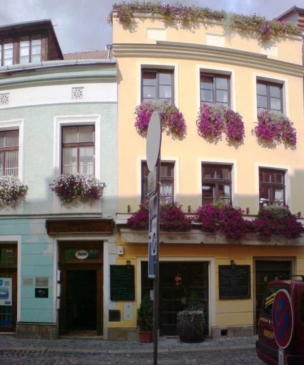 A building with multiple windows, some with flower boxes. There is a sign on the building and a red vehicle parked in front.