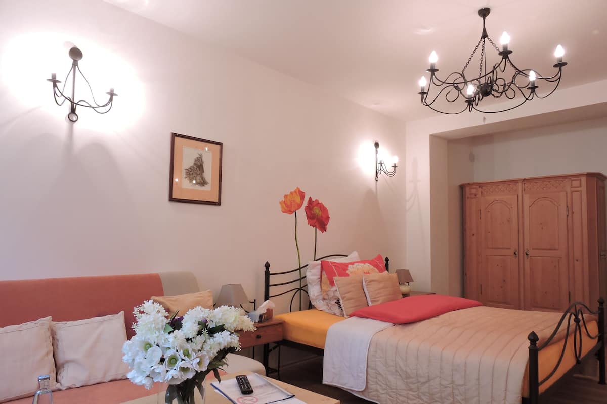 A bedroom with a bed, a sofa, a nightstand, a vase of flowers, a framed picture, and a wardrobe.