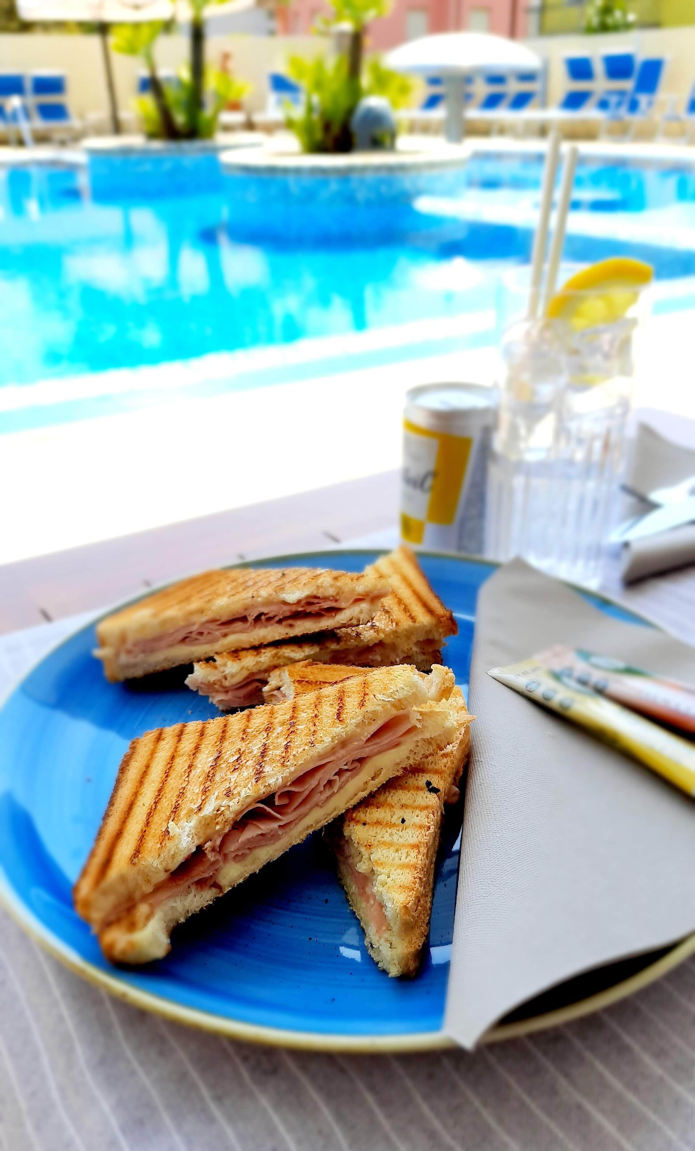 A plate with grilled sandwiches, a drink, and a menu on a table by a pool.