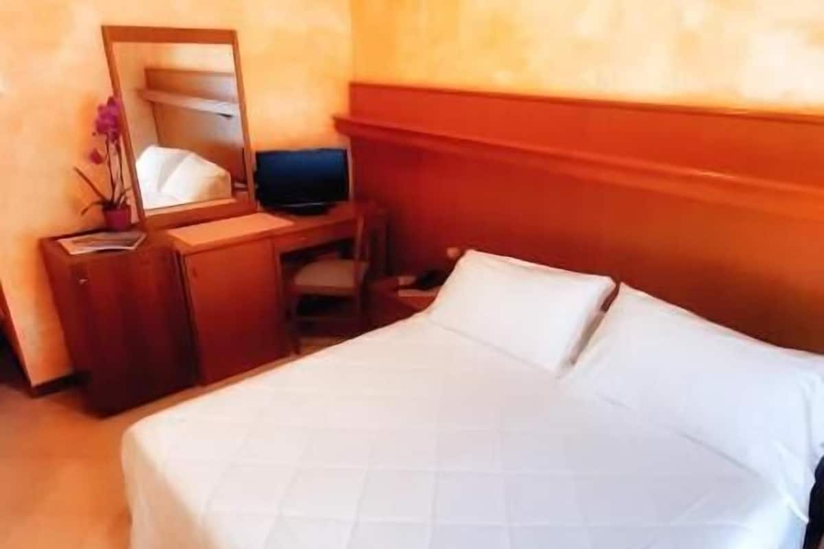 Une chambre d’hôtel avec un lit, un bureau, une chaise et un miroir.