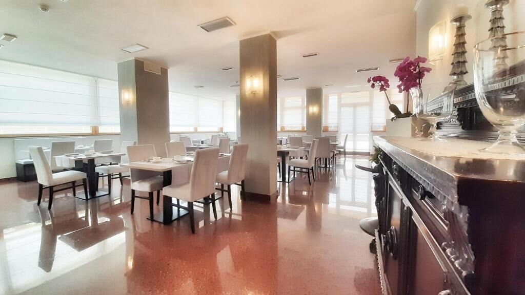 A spacious dining area with multiple tables and chairs, large windows, and a polished floor.