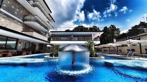 Una piscina con una fuente de agua, sillas de descanso y vista a un edificio con balcones.