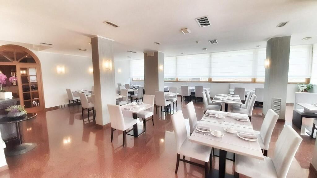 A spacious dining area with multiple tables and chairs, large windows, and a polished floor.