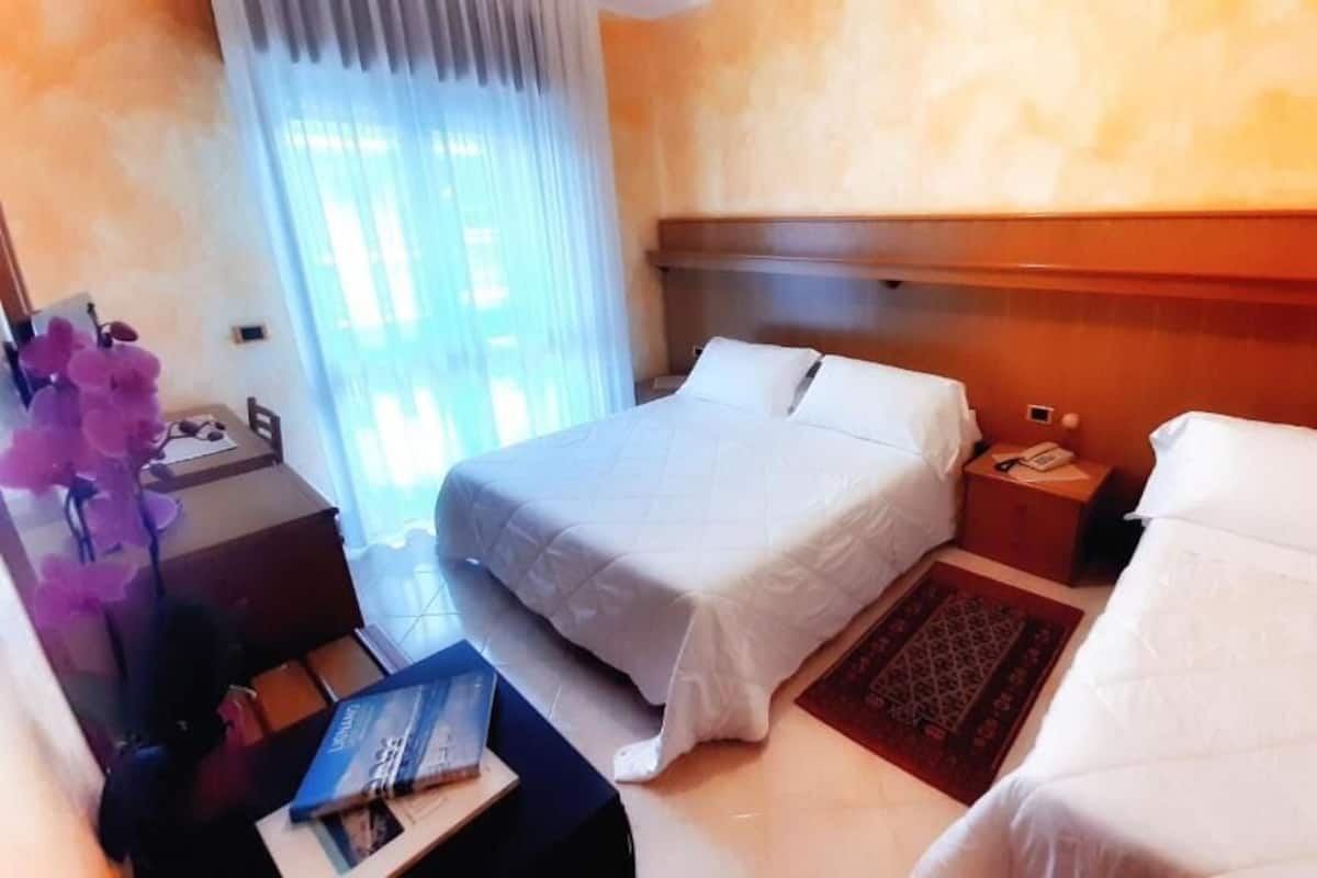 Une chambre d’hôtel avec deux lits, un bureau, une chaise, une petite table et une fenêtre avec des rideaux.