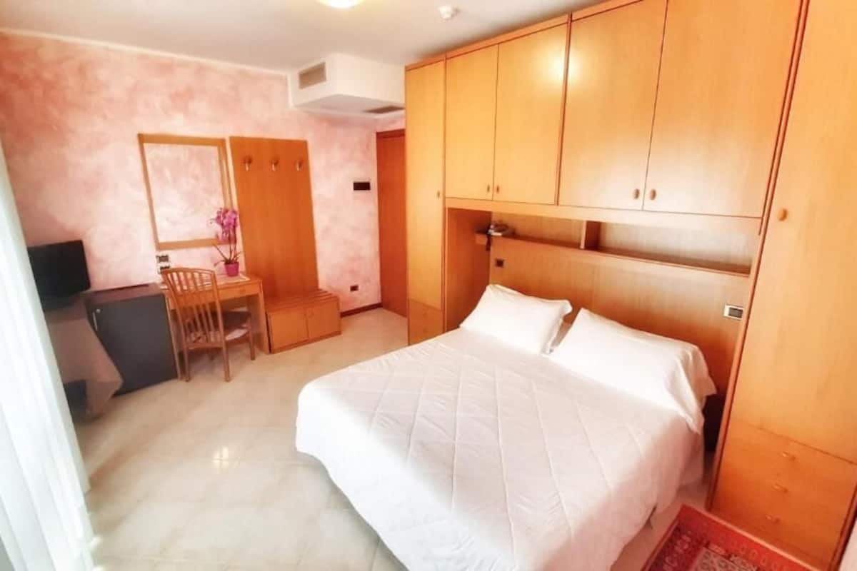 Une chambre à coucher comprenant un lit, une armoire en bois, un bureau, une chaise et une petite table sur laquelle est posée une plante en pot.