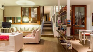 Un salon moderne avec un canapé, une table basse et un téléviseur. Un escalier mène à un autre niveau.
