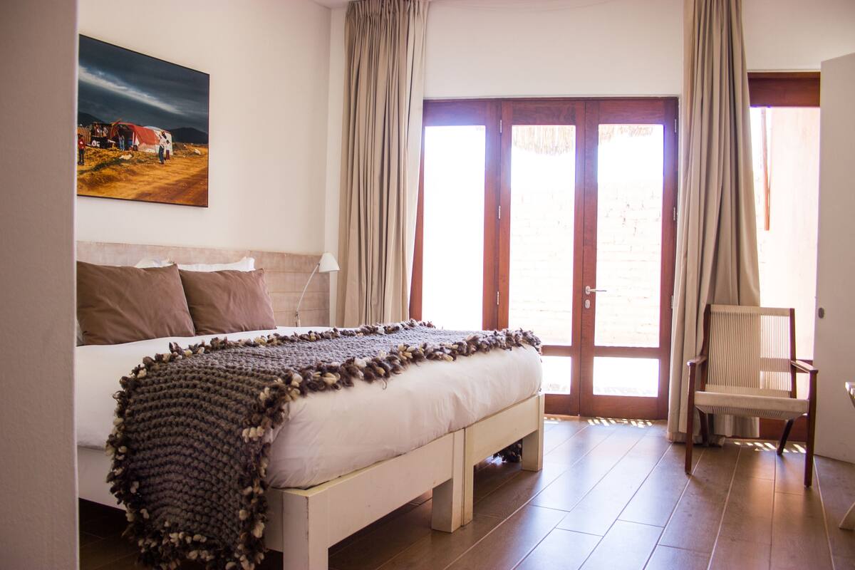 Een slaapkamer met een bed, een stoel, een schilderij aan de muur en een deur die uitkomt op een buitenruimte.