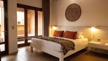 Une chambre avec un grand lit, une table de chevet, une lampe fixée au mur et une vue sur l’extérieur, visible à travers une porte vitrée.