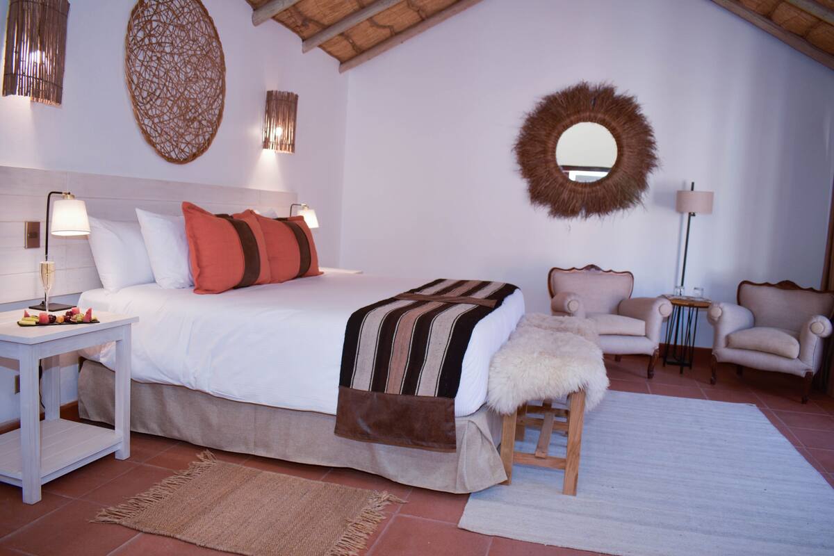 Een slaapkamer met een groot bed, twee stoelen, een tafeltje en een spiegel aan de muur.