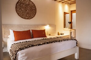 A bedroom with a bed, pillows, a bedside lamp, a mirror, and a small bedside table.
