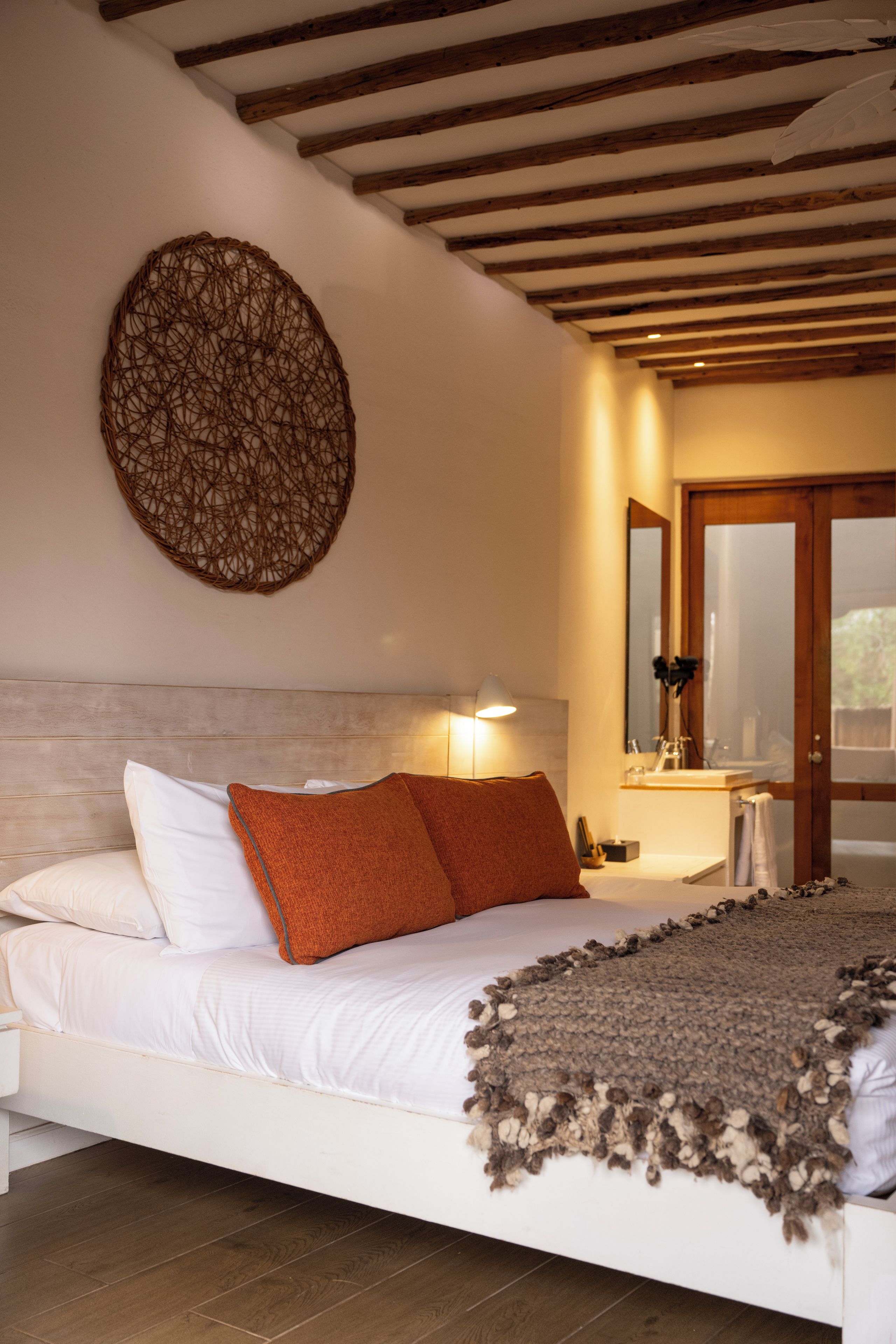 Un dormitorio con cama, almohadas, una obra de arte colgada en la pared, una lámpara de noche y una puerta de madera.
