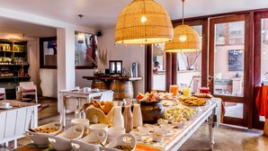 A breakfast buffet with various food items and beverages, a bar area with bottles and glasses, and a cozy seating area with a fireplace. - Noi Casa Atacama (San Pedro de Atacama)