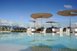 Piscina infinita no terraço com espreguiçadeiras e guarda-sóis, com vista para o horizonte urbano.