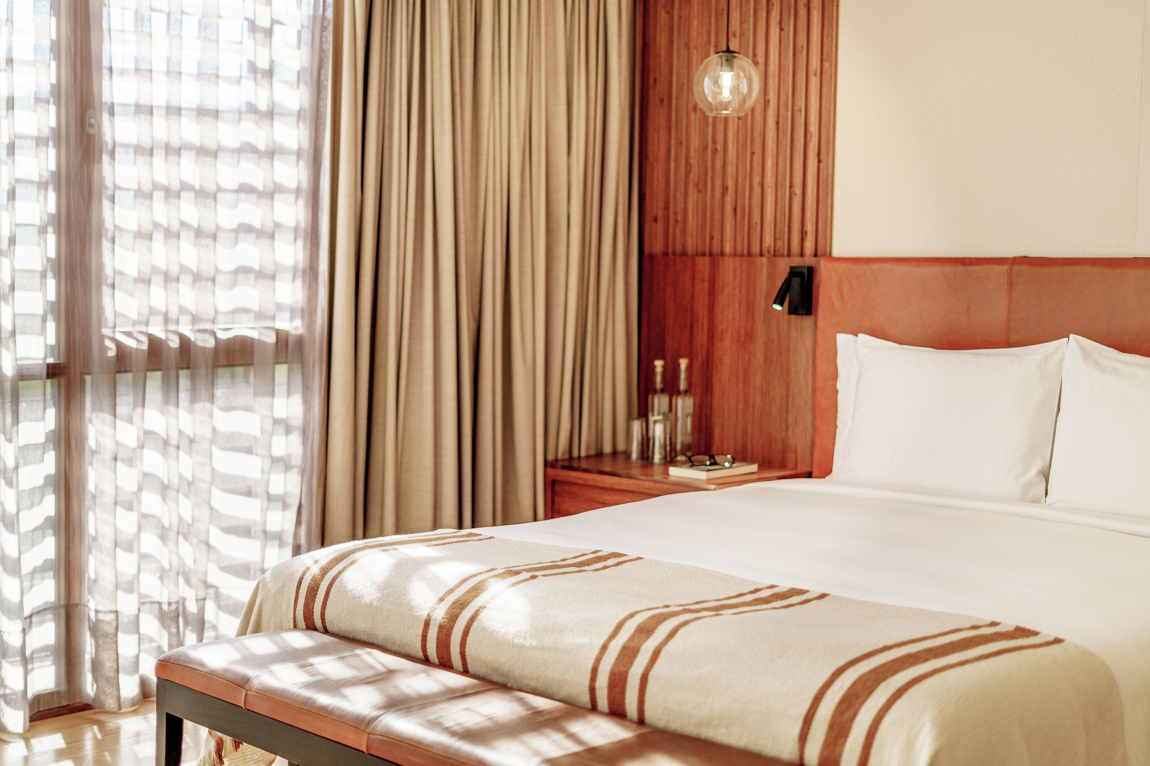 Habitación de hotel con cama, una banca, una mesita de noche y una lámpara fijada a la pared.
