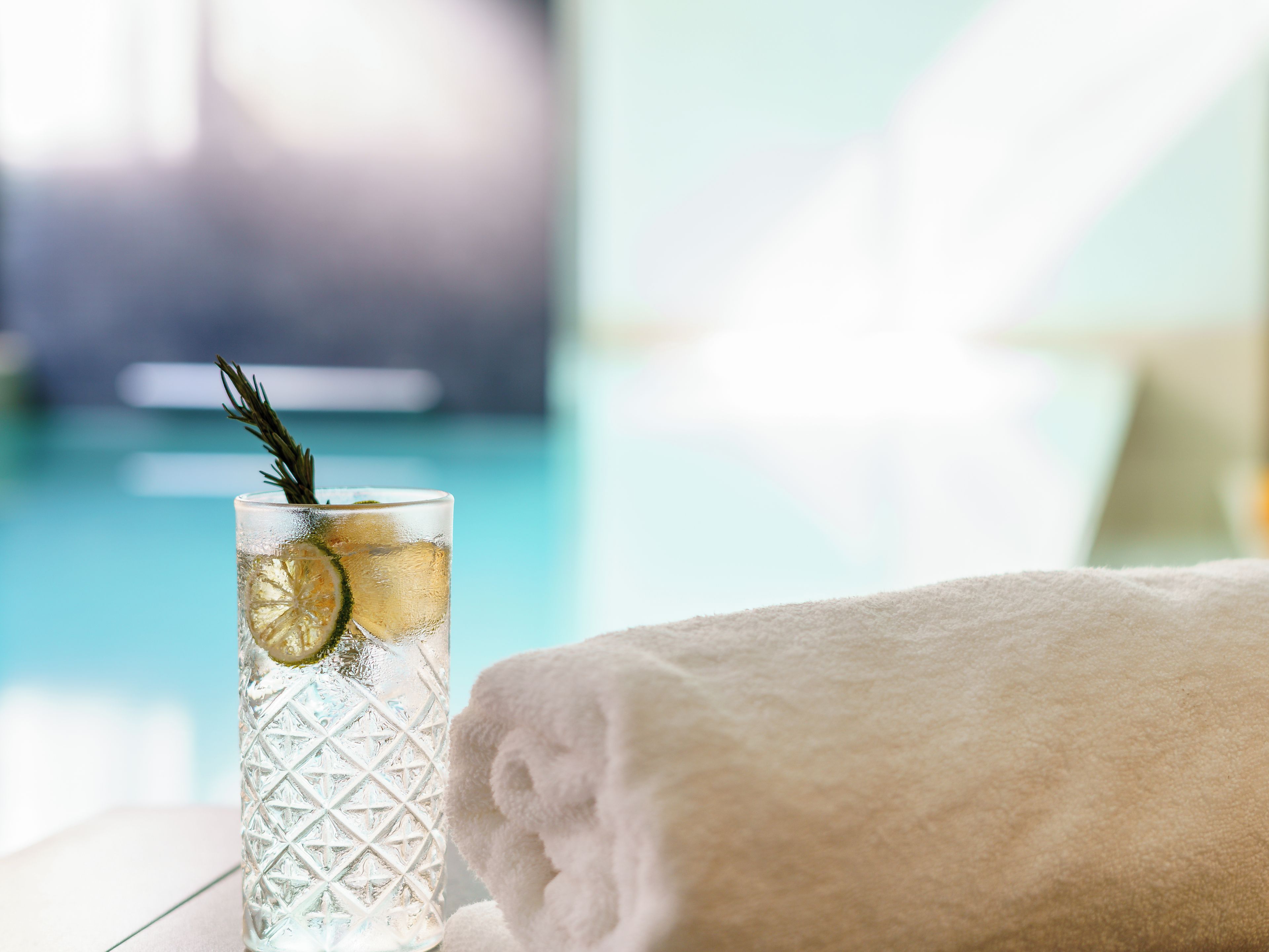 A clear glass with a lemon slice and a sprig of rosemary, placed on a reflective surface next to a neatly folded white towel.
