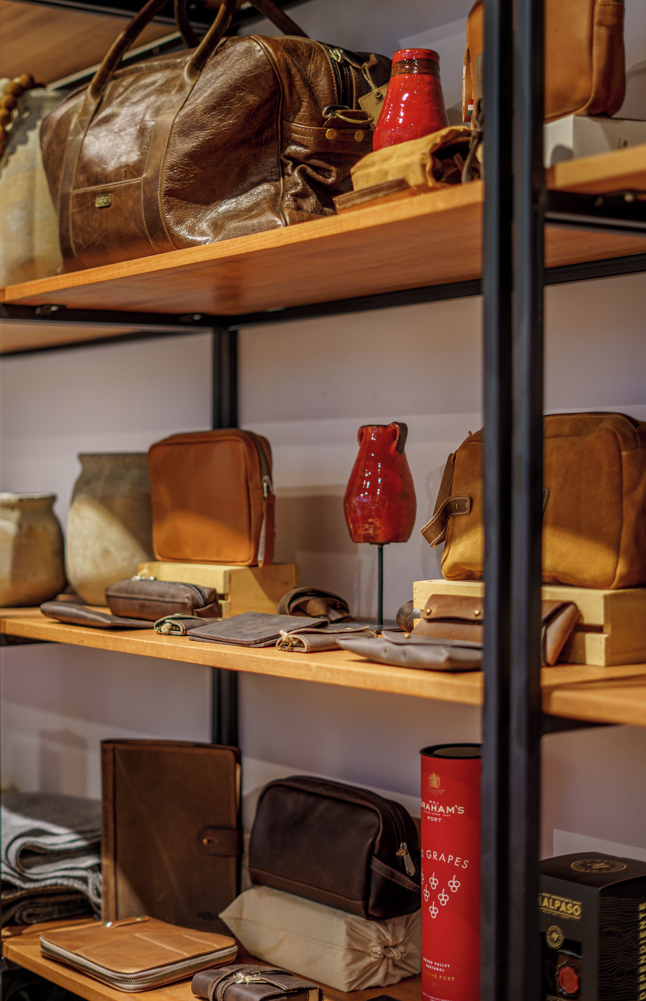 Shelves with various leather bags and a red vase.