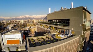 Un edificio moderno con jardín en la azotea, amplias ventanas y vistas a un paisaje urbano con montañas al fondo.