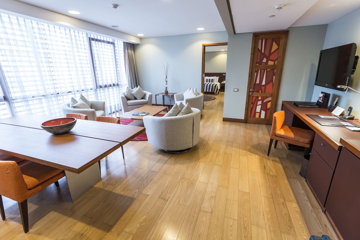 Une chambre d’hôtel moderne dotée d’un coin repas, d’un espace salon avec des canapés, d’une télévision et d’un plancher en bois.