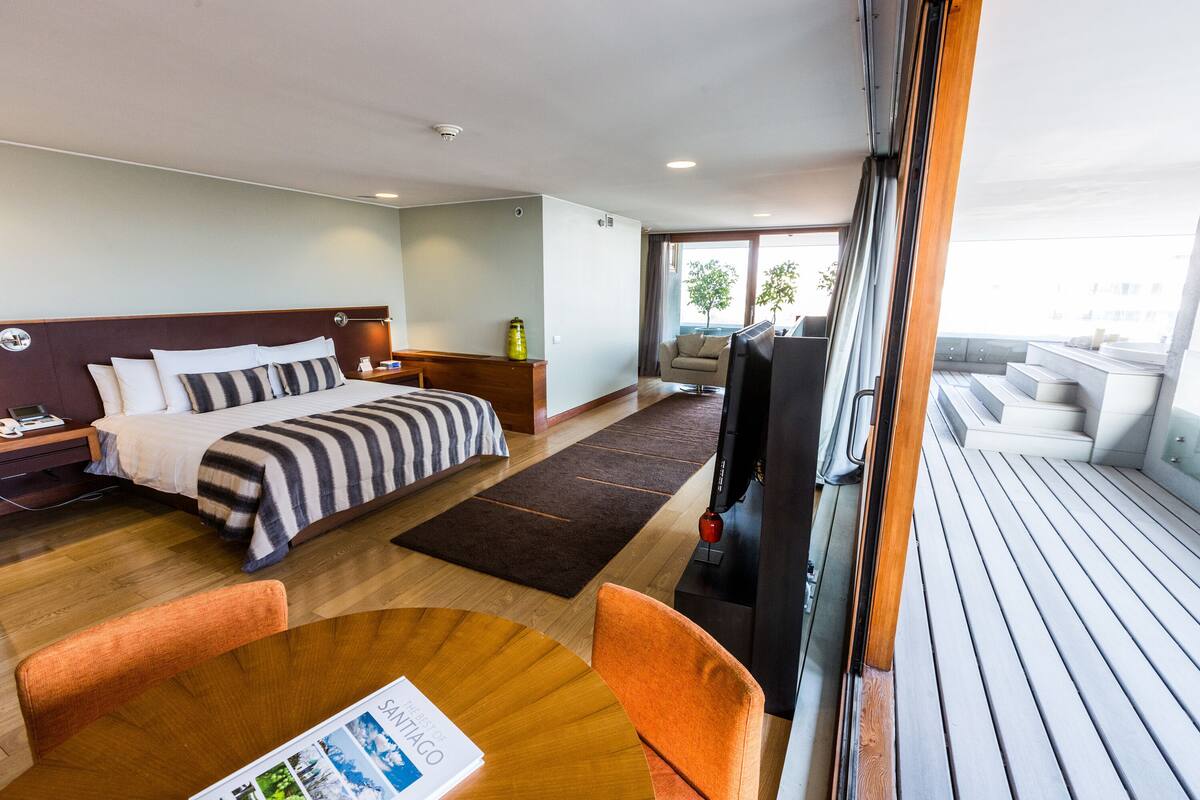 Une chambre d’hôtel avec un lit, une télévision, un plancher en bois, un canapé et un balcon avec vue.