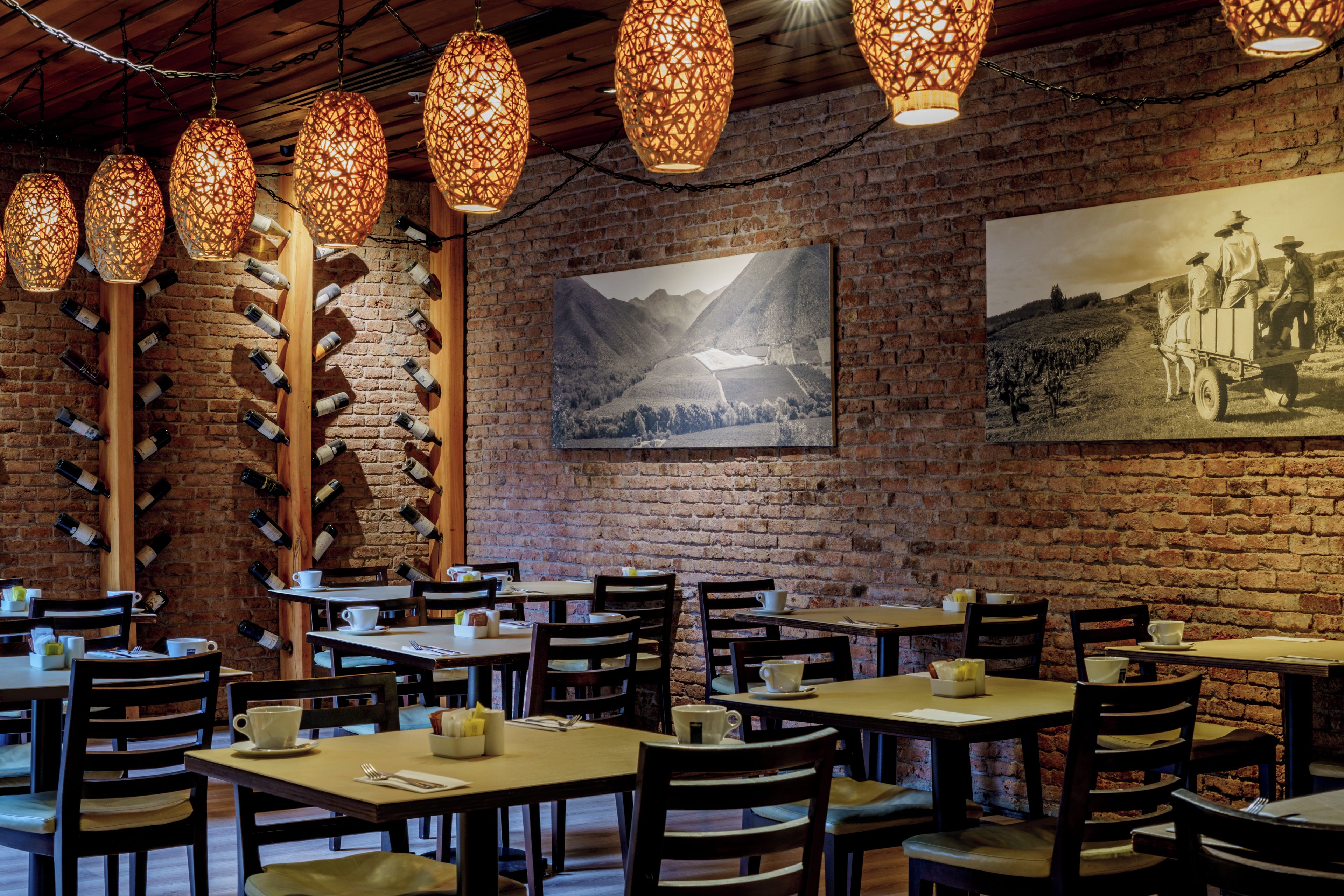Een restaurantinterieur met bakstenen muren, houten tafels en hangende lampen.