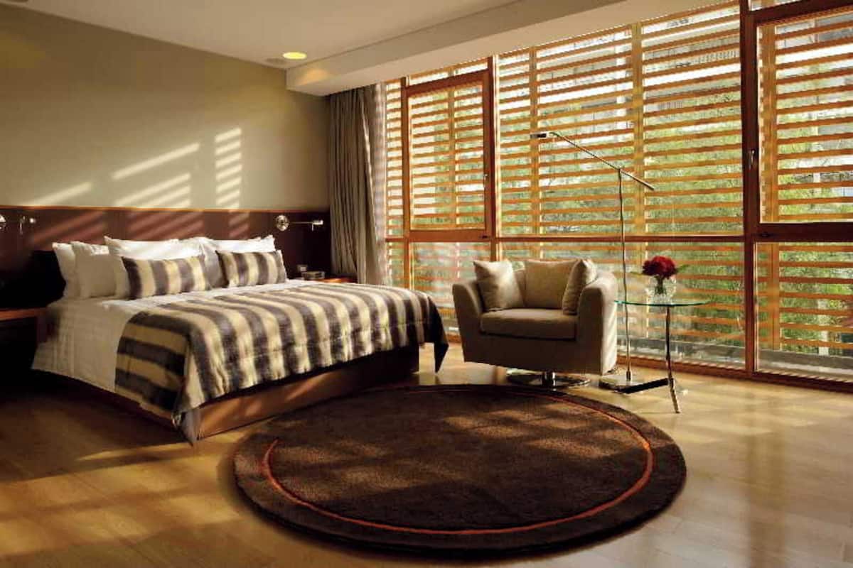Une chambre à coucher comprenant un lit, une chaise, un tapis rond et de grandes fenêtres équipées de stores.