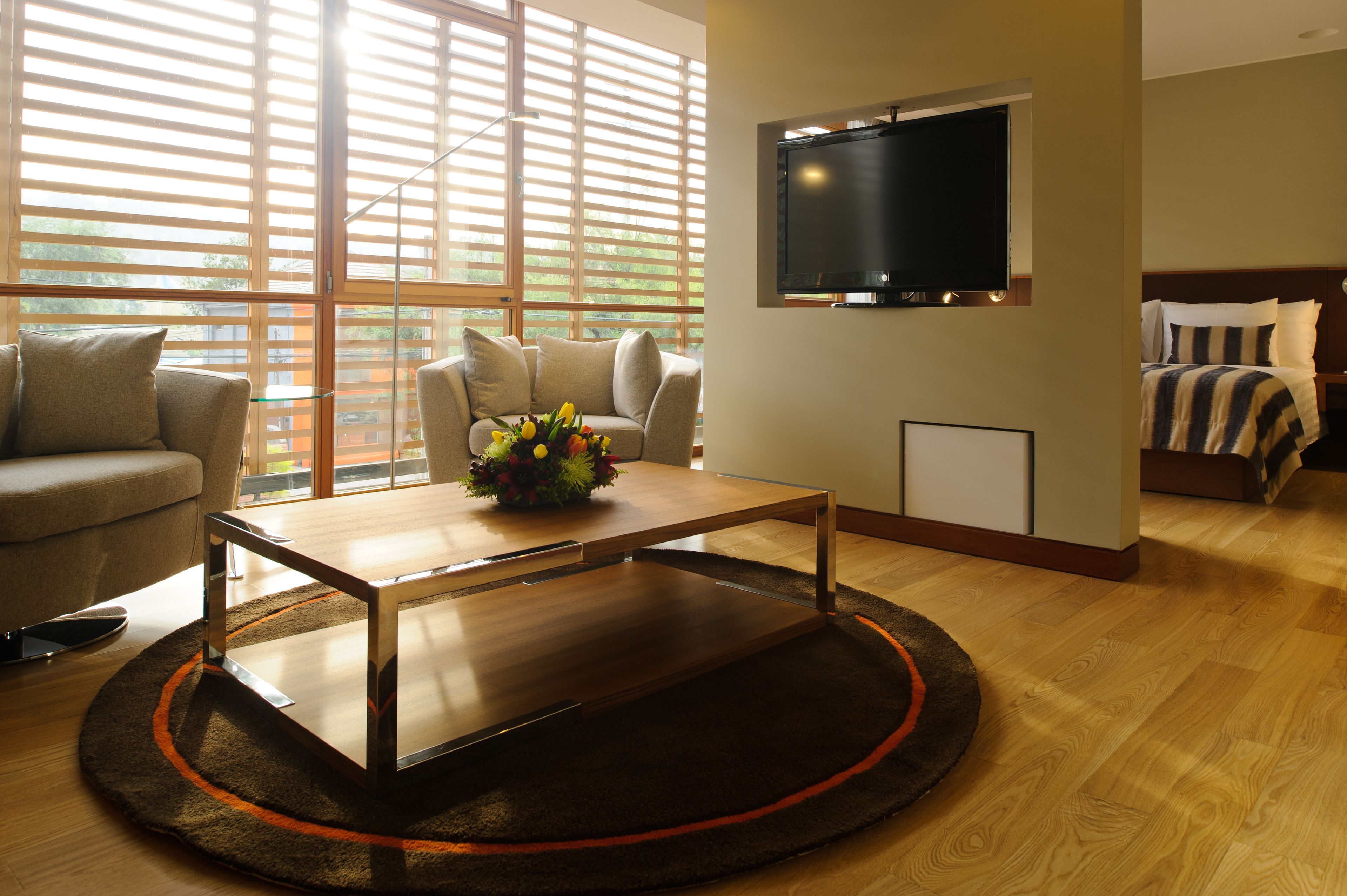 Uma sala de estar moderna com uma mesa de centro de madeira, um sofá, uma TV fixada na parede e uma cama com roupa de cama listrada.