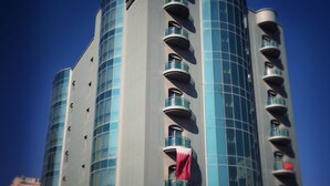 A modern hotel with a curved facade, multiple balconies, and a prominent signage at the top. - Al Madina Suites Doha (Doha)