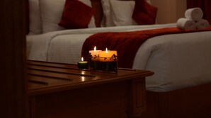 A hotel room with a bed, a nightstand with candles, and a wall-mounted lamp. - Al Madina Suites Doha (Doha)