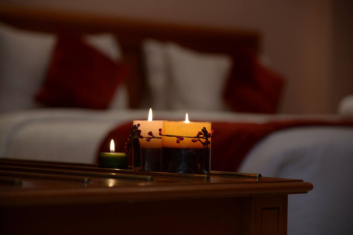 Una mesita de noche con una vela encendida y otra vela más pequeña en un soporte de vidrio.