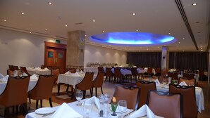 A dining area with multiple tables set for service, chairs, and a central light fixture. - Al Madina Suites Doha (Doha)