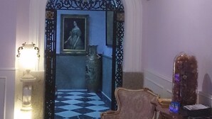 Una habitación con piso de tablones, una araña, un retrato enmarcado y una cruz en la pared.