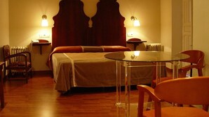 Habitación de hotel con cama, una mesita de vidrio, dos sillas, un radiador y dos lámparas fijadas a la pared.