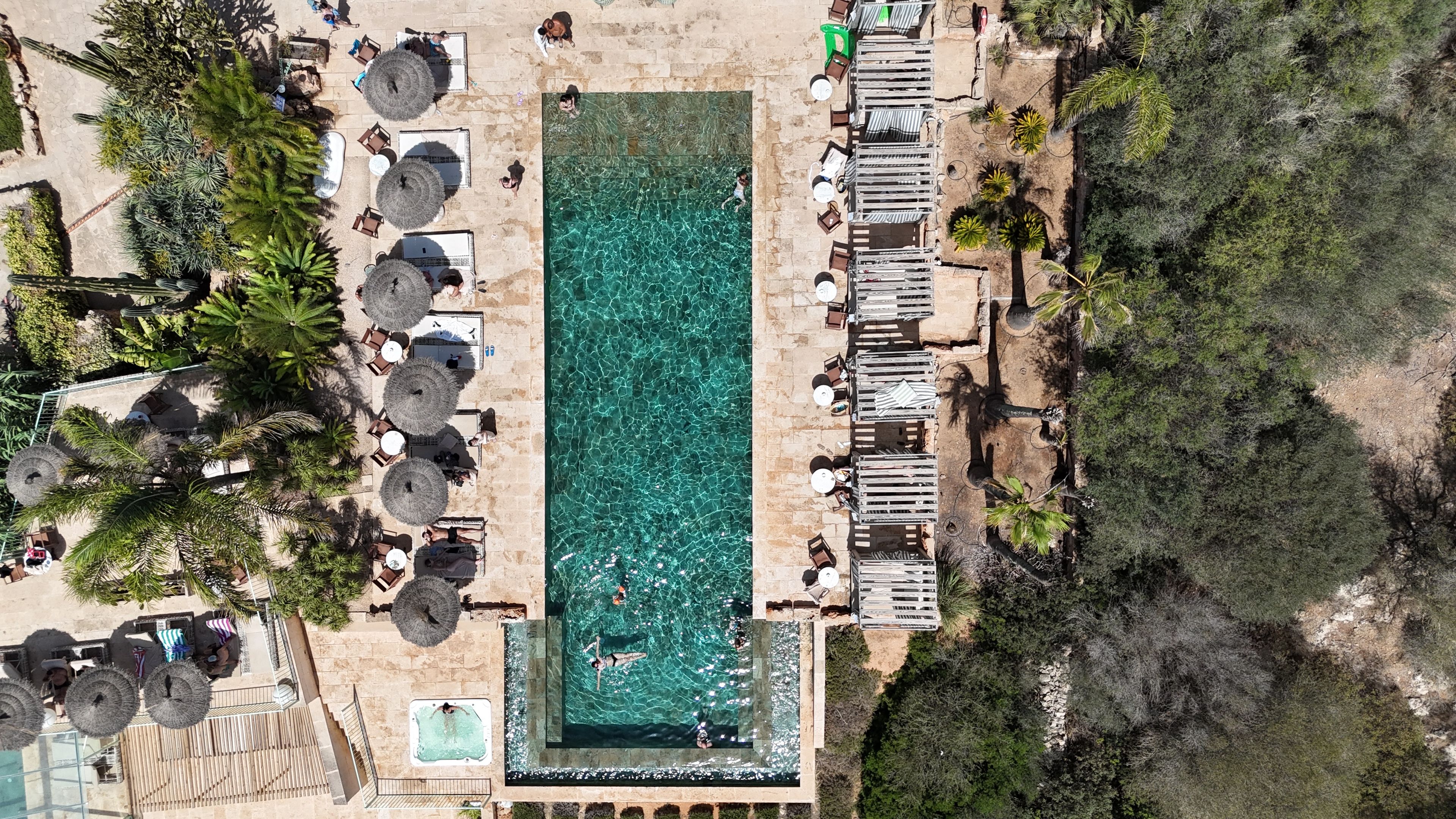 Vue aérienne d’un complexe hôtelier avec une piscine, des chaises longues et des palmiers.