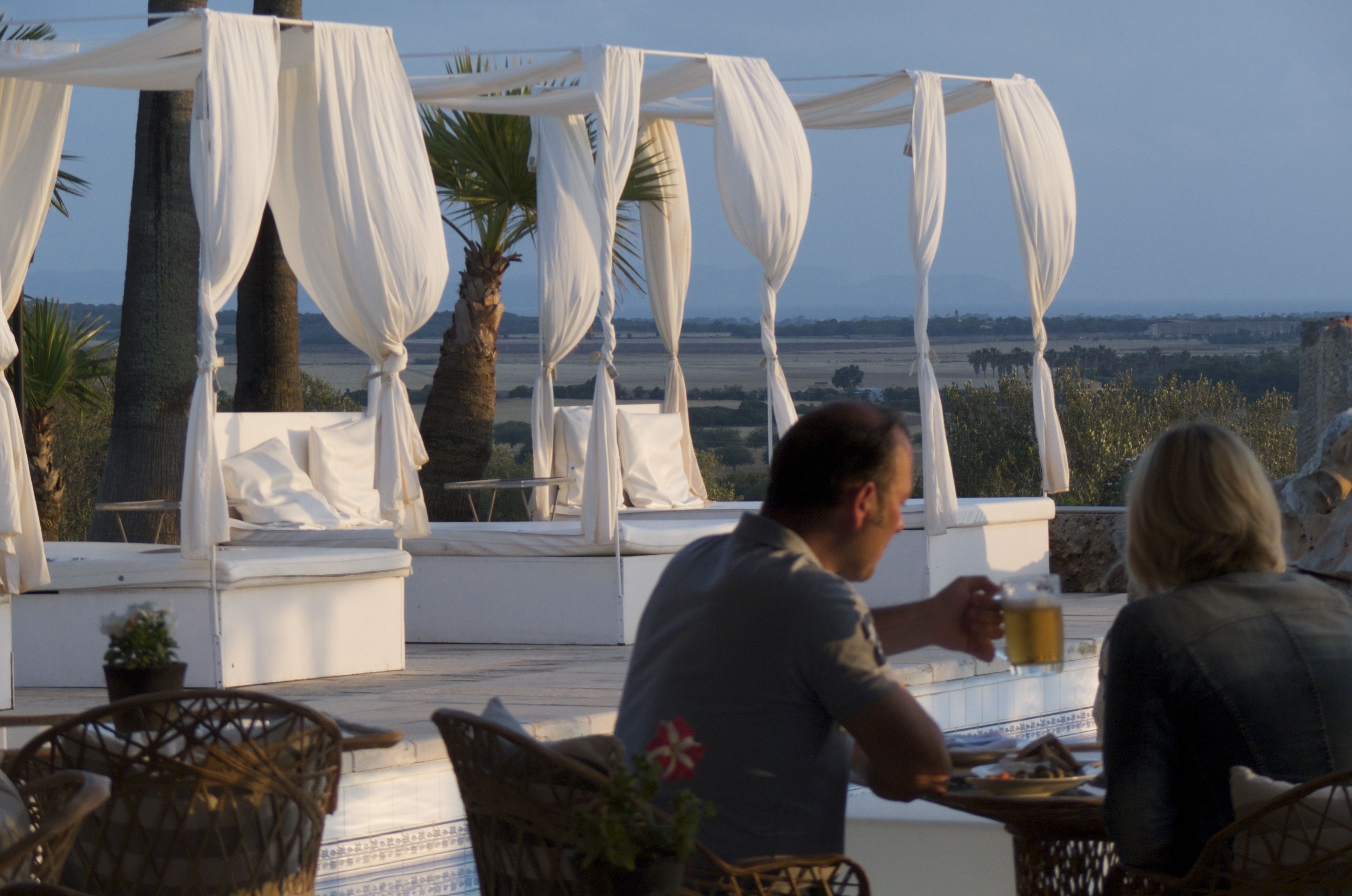 A terrace with a white canopy, wicker chairs, and a table with drinks.