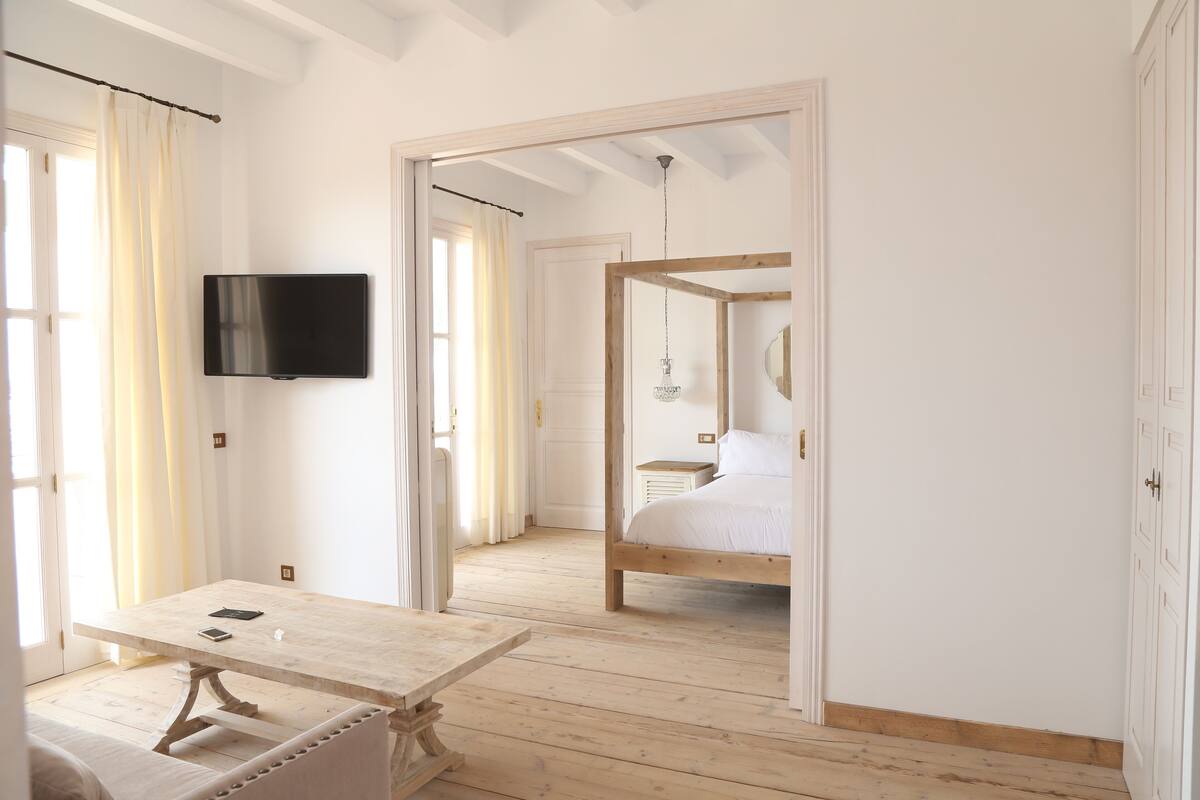 Quarto com cama de madeira, televisão presa na parede e mesa com cadeira.