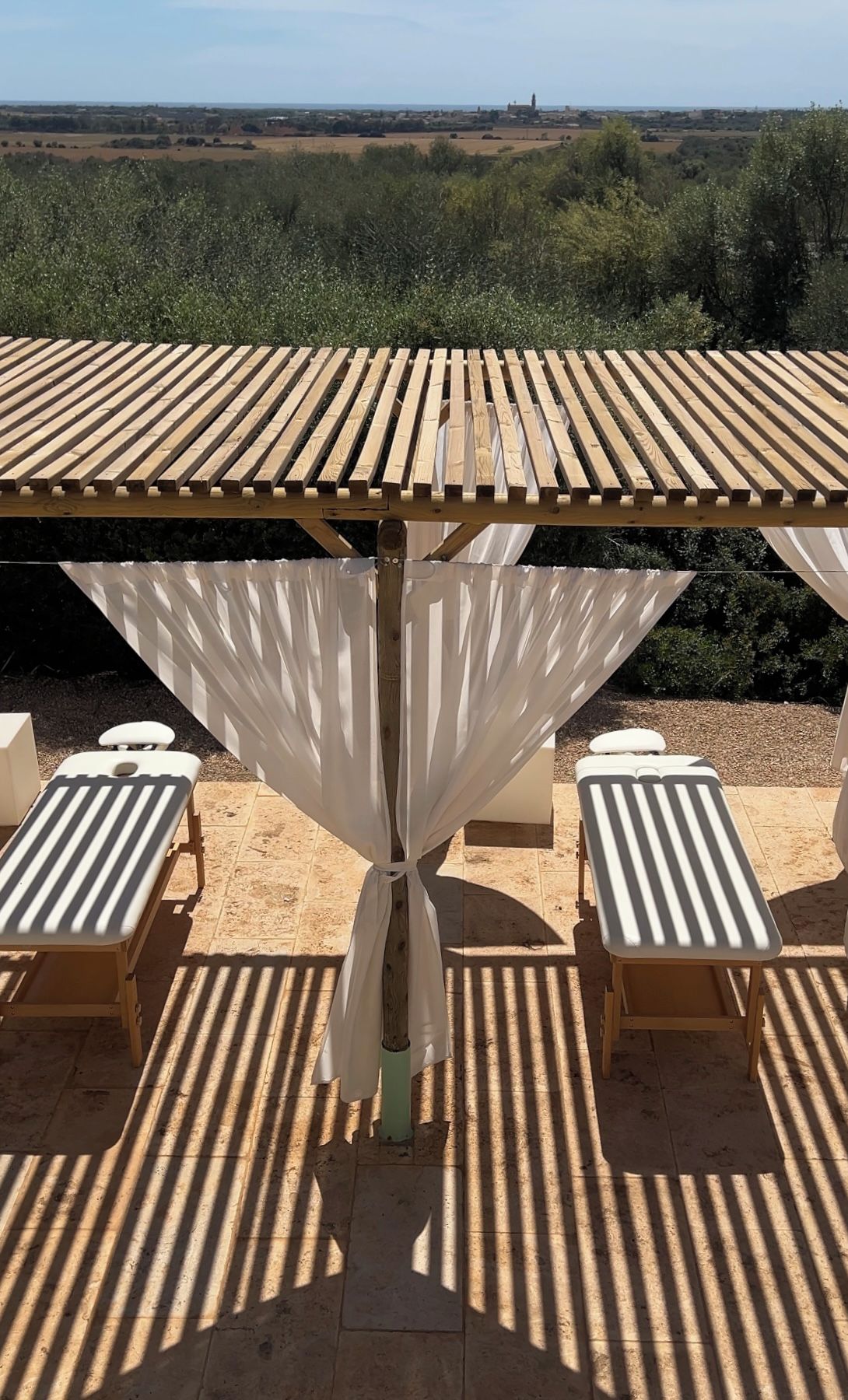 Une table en bois surmontée d’un parasol blanc, entourée de quatre fauteuils de jardin blancs.