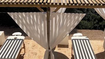 Une table en bois surmontée d’un parasol blanc, entourée de quatre fauteuils de jardin blancs.