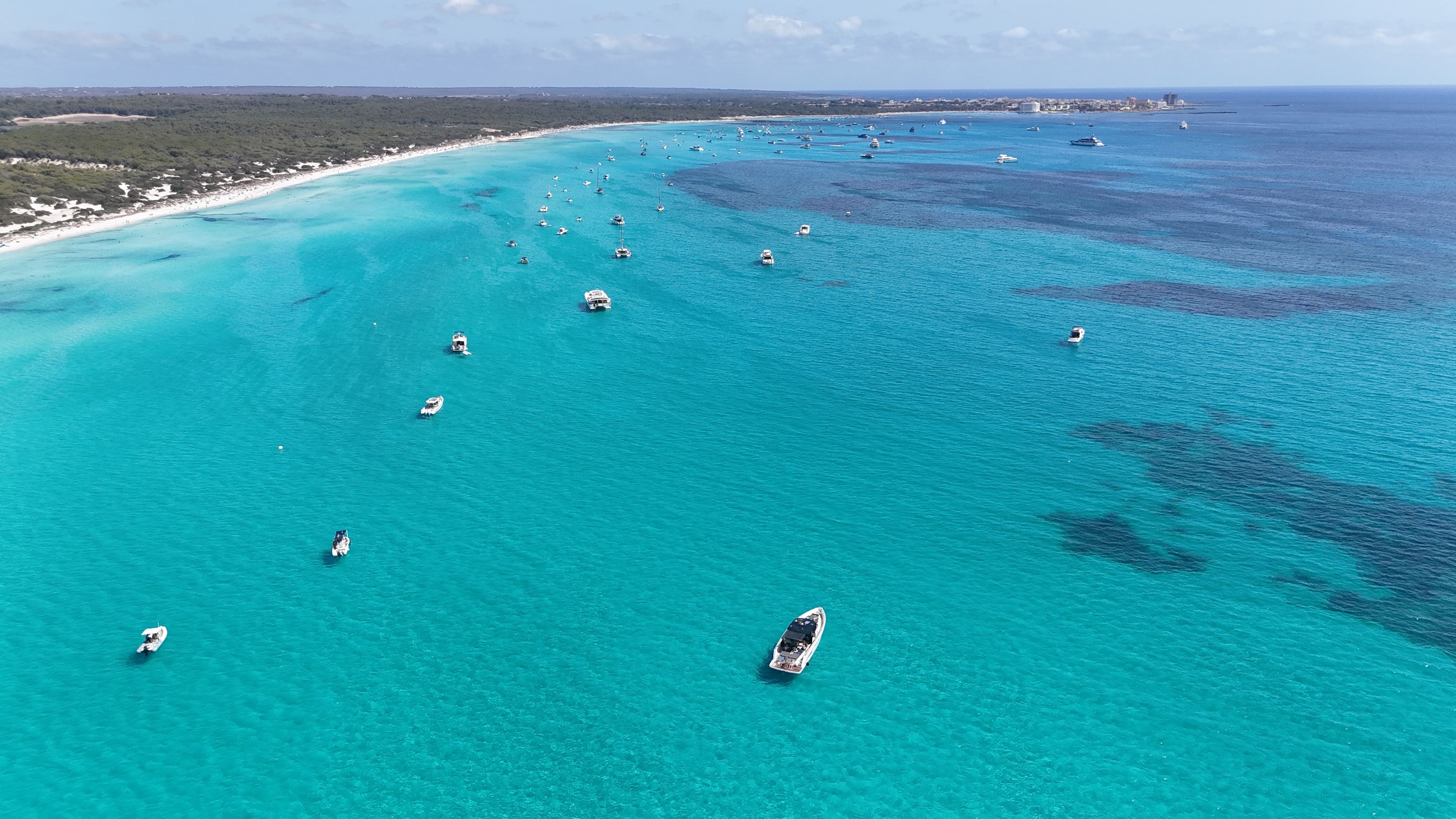 Vue aérienne d’une zone côtière avec des eaux turquoise limpides, des bateaux et une plage.