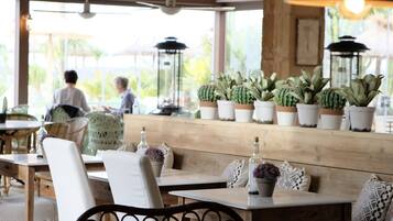 A restaurant with wooden tables and chairs, potted plants, and a view of the outdoors.
