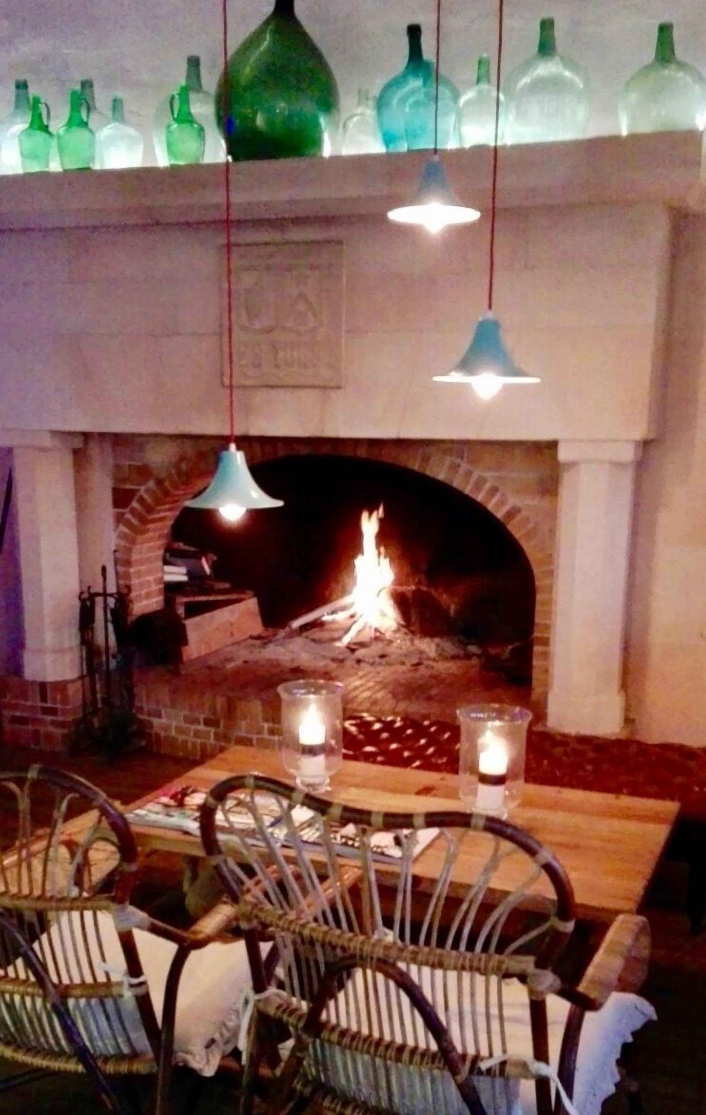 Interior de restaurante com lareira de tijolos, luminárias pendentes e uma mesa posta para refeição.