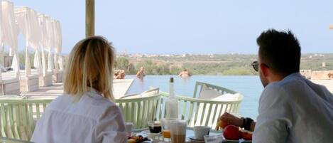 Two people dining at a table with a view of a pool and a distant landscape.