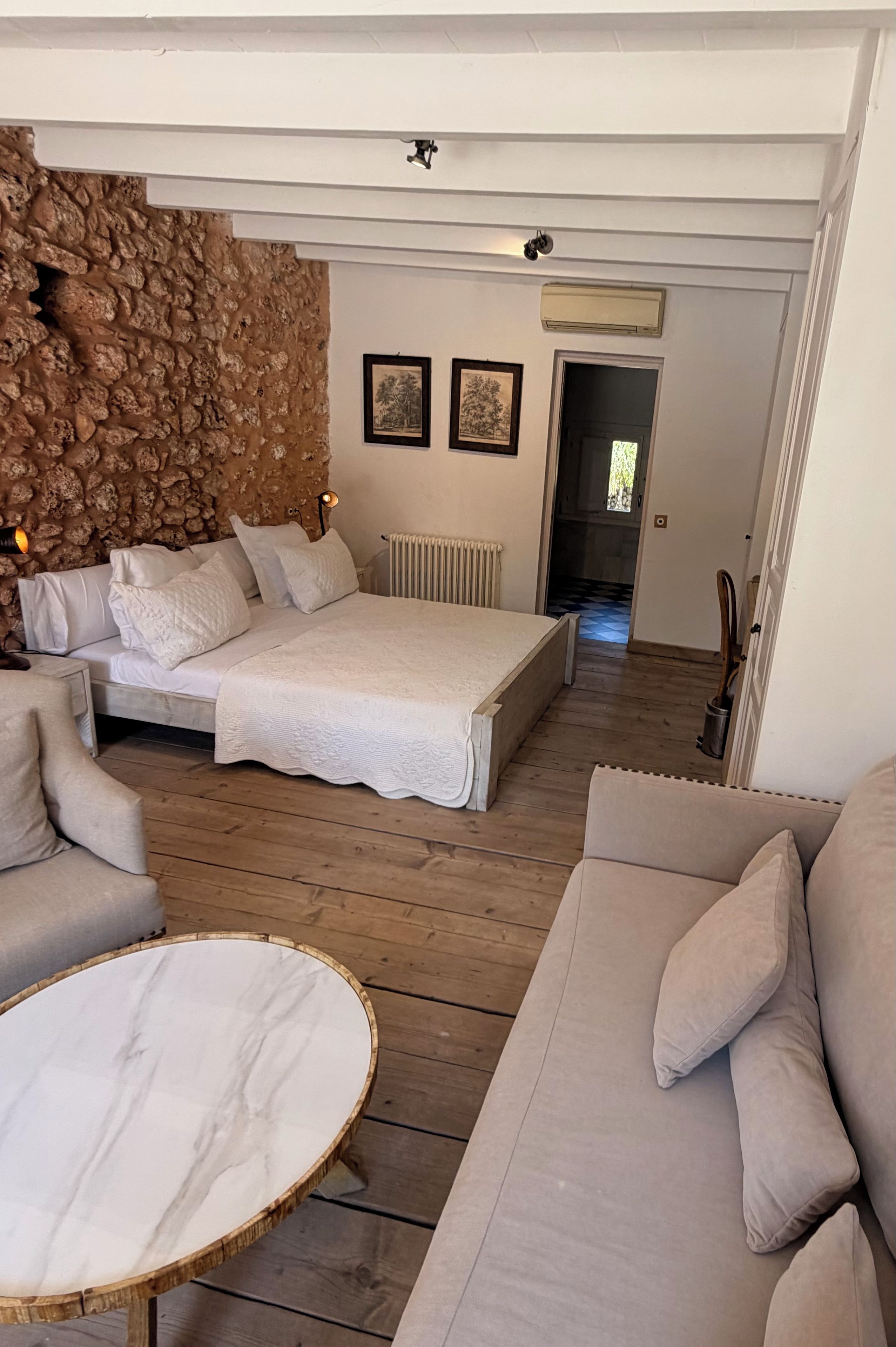 A bedroom with a bed, a sofa, a round table, and a stone wall.