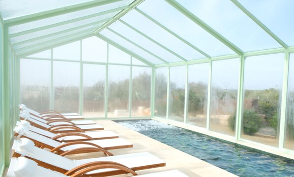 A greenhouse with a pool, lounge chairs, and a view of the outdoors.