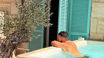 Un homme se détend dans un bain à remous, avec un arbre et un bâtiment en arrière-plan.